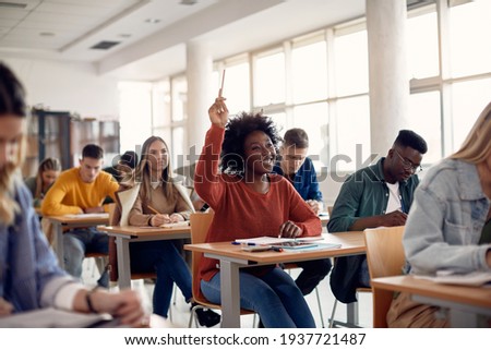 Happy African American student raising her hand to ask a question during lecture in the classroom. 