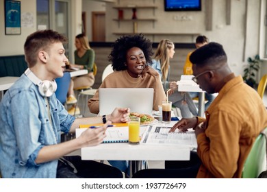 Happy African American Student Using Laptop And Talking To Her Friends At University Cafeteria. 