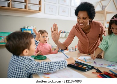Happy African American teacher and small boy giving high-five during art class at kindergarten.  - Shutterstock ID 2121874898