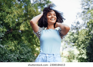 Happy african american teen girl in casual cloth. Smiling darkskin female teenager walking in the park. Summer time. Green trees on background. Copy space. - Powered by Shutterstock