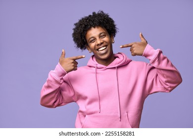 Happy African American teen guy pointing at dental white teeth advertising whitening. Smiling student showing healthy teeth perfect natural orthodontic smile standing isolated on purple background. - Powered by Shutterstock