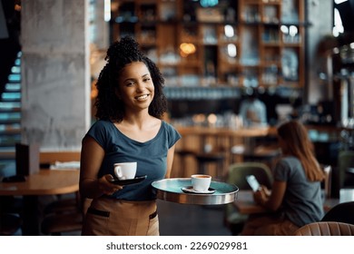 Happy African American waitress serving coffee while working in cafe ad looking at camera. - Powered by Shutterstock