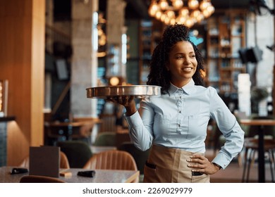 Happy African American waitress working in restaurant and looking away. - Shutterstock ID 2269029979