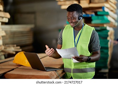 Happy African American warehouse worker analyzing reports during video call over laptop. - Powered by Shutterstock