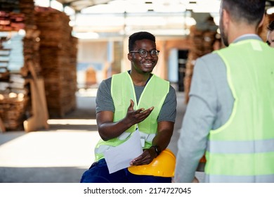 Happy African American warehouse worker talking to a businessman at timber storage compartment. - Powered by Shutterstock