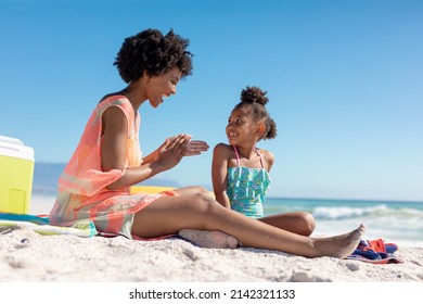 Happy african american woman applying suntan lotion on daughter while sitting at beach on sunny day. unaltered, family, lifestyle, togetherness, enjoyment and holiday concept. - Powered by Shutterstock