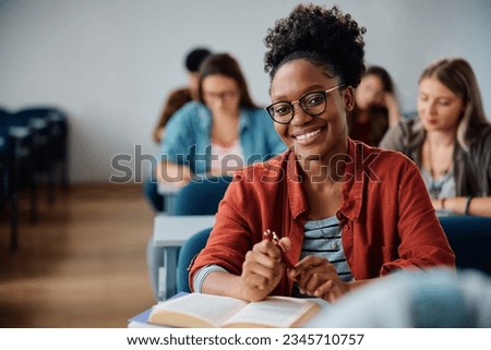 Happy African American woman attending a lecture in university classroom and looking at camera.