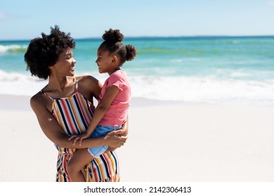 Happy african american woman carrying daughter while standing at beach on sunny day. unaltered, family, lifestyle, togetherness, enjoyment and holiday concept. - Powered by Shutterstock