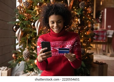 Happy African American woman do shopping use smartphone and credit card on New Year winter season sales. Smiling biracial female order online on cellphone, buy on Christmas discounts on web. - Powered by Shutterstock