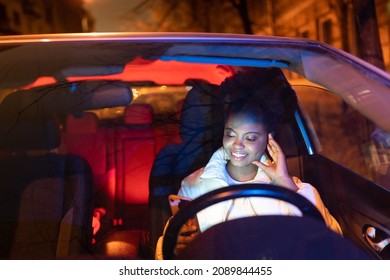 Happy African American Woman Driver Using Mobile, Looking At Phone Screen Surfing Internet, Afro Female Texting, Chatting And Online Messaging In Social Media While Sitting In Car With Smartphone