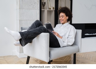 happy african american woman in earphones holding digital tablet while watching movie and sitting on grey armchair - Powered by Shutterstock