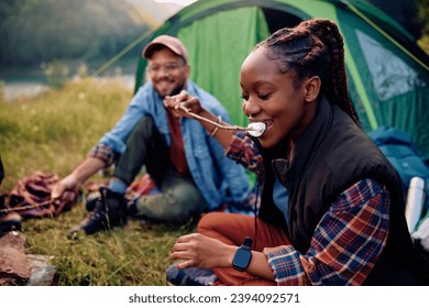 Happy African American woman eating roasted marshmallows while camping with her boyfriend. - Powered by Shutterstock