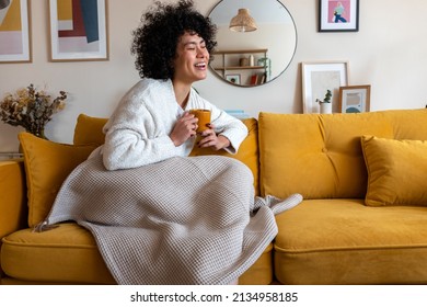 Happy African american woman enjoying quiet time at home laughing, drinking morning coffee sitting on sofa. Copy space. - Shutterstock ID 2134958185