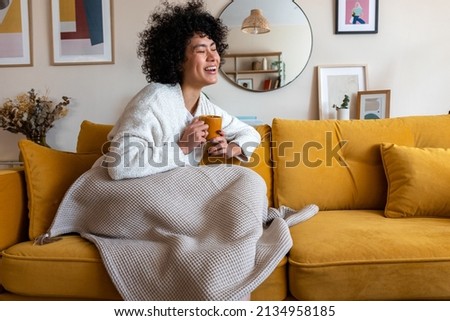 Happy African american woman enjoying quiet time at home laughing, drinking morning coffee sitting on sofa. Copy space.