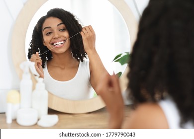 Happy African American Woman Flossing Her Teeth With Dental Floss In Front Of Mirror At Home, Enjoying Her Perfect White Smile