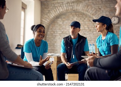 Happy African American woman and group of volunteers sharing duties and talking while organizing donations at charity center. - Shutterstock ID 2147202131