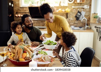 Happy African American woman having Thanksgiving lunch with her family and serving salad at dining table.  - Shutterstock ID 1839418558