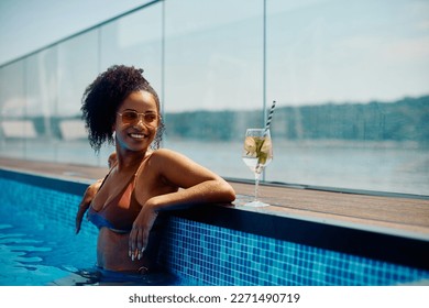 Happy African American woman having a cocktail while enjoying in the swimming pool on summer day.  - Powered by Shutterstock