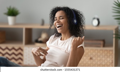 Happy African American woman in headphones listening to music, beautiful girl singing favorite song, imagine playing guitar, attractive female having fun at home, enjoying melody - Powered by Shutterstock