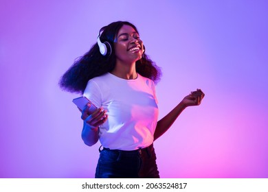 Happy African American woman with headphones and smartphone listening to music and dancing in neon light. Young black woman moving to favorite song, enjoying cool playlist - Shutterstock ID 2063524817