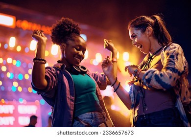 Happy African American woman and her female friend having fun and dancing while attending open air music concert at night. - Powered by Shutterstock