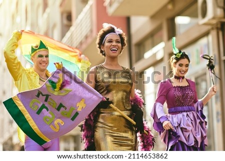 Happy African American woman and her friends in carnival costumes and make-up on Mardi Gras parade. 
