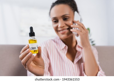 Happy African American Woman Holding Bottle With Cbd And Talking On Smartphone