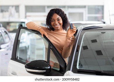 Happy African American Woman Holding Keys To New Car And Smiling At Camera, Excited Black Female Posing Near Her Vehicle In Dealership Center Or Rental Office, Leaning On Automobile Door, Free Space
