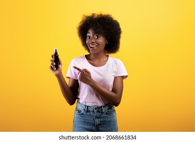 Happy African American Woman Holding And Pointing At Spray, Demonstrating New Hair Care Product And Smiling, Posing Over Yellow Color Studio Background