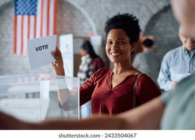 Happy African American woman inserting her ballot in voting box at polling place during US elections.  - Powered by Shutterstock