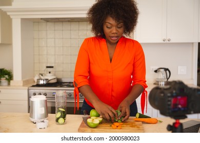 Happy African American Woman In Kitchen Preparing Health Drink, Making Vlog Using Laptop And Camera. Online Cookery Vlogger At Home.