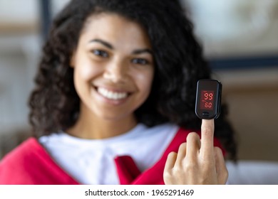 Happy African American Woman Measures  Pulse And Oxygen Saturation Using A Pulse Oximeter Sitting On The Couch At Home, Healthcare Concept