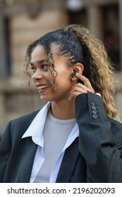 happy african american woman in oversize suit adjusting wireless earphone on urban street of prague - Shutterstock ID 2196202093