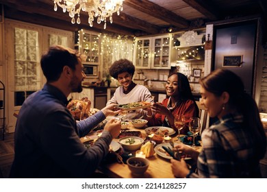 Happy African American Woman Passing Food While Having Thanksgiving Meal With Friends At Dining Table. 