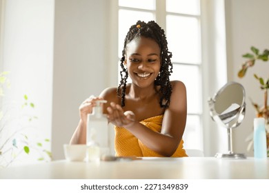 Happy african american woman pouring moisturising body lotion from bottle on hand, sitting wrapped in towel, using new skincare product after bath, free space - Powered by Shutterstock