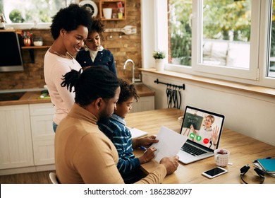 Happy African American woman reminding her husband to finish with work on laptop so that kids could follow online classes at home. 