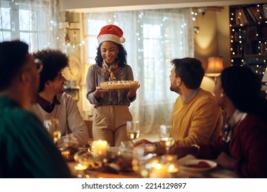Happy African American woman serving sweet pie to her friends during Christmas lunch at home. 