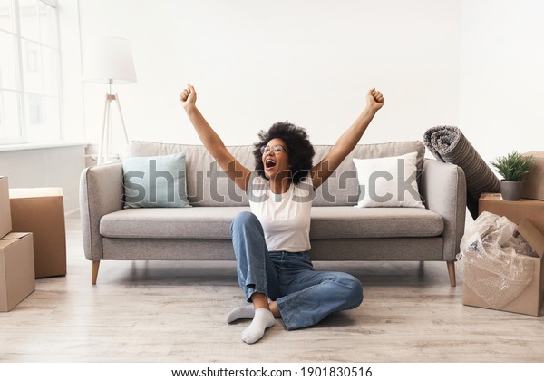 Happy African American\
Woman Sitting Among Moving Boxes Indoor, Shaking Fists Celebrating\
Relocation To New Home. Real Estate, Renting Apartment Service,\
Housing Concept