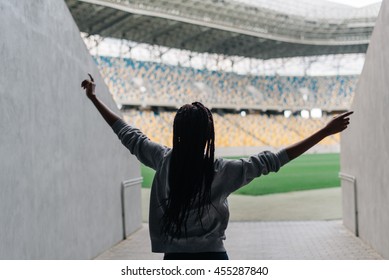 Happy African American Woman Standing Among Empty Stadium Celebrating, Her Arms Raised Punching The Air With Hands, View From Back