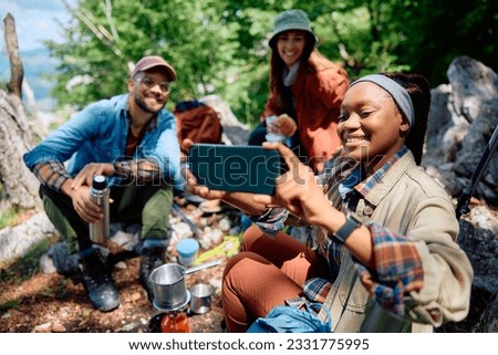 Happy African American woman taking selfie with her friends while camping in nature.