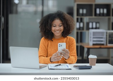 Happy African American woman talking on the smartphone with laptop at office desk. - Powered by Shutterstock