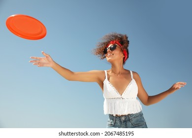 Happy African American woman throwing flying disk against blue sky on sunny day