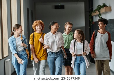 happy african american woman walking with teenage students in hallway of school, teacher and kids - Powered by Shutterstock