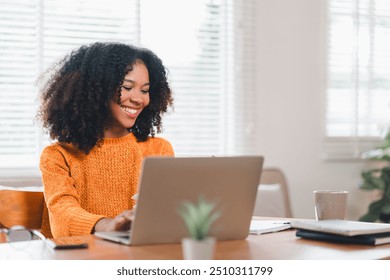 Happy African American woman wearing glasses working on laptop at home - Powered by Shutterstock