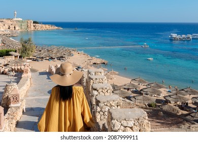 Happy African American woman in yellow dress and sun hat enjoys view of coast of Red Sea on natural background. Panoramic views of blue sea with yachts and coastline, Sharm El Sheikh, Egypt.  - Shutterstock ID 2087999911