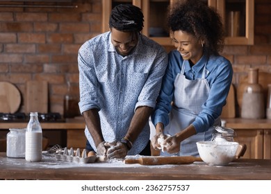 Happy African American young couple kneading dough, standing at table in kitchen together, smiling woman and man cooking baking at home, wife and husband cooking pastry or cookies, enjoying weekend - Powered by Shutterstock