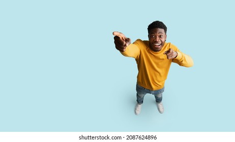 Happy african american young man in casual showing copy space, pointing at blank space for advertisement or text, blue studio background, panorama, top view, full length shot - Shutterstock ID 2087624896