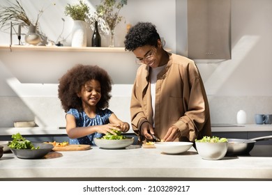 Happy African American young mom and daughter girl preparing dinner together, slicing fresh vegetables at kitchen table, cooking from natural healthy food ingredients, chatting, talking, having fun - Powered by Shutterstock