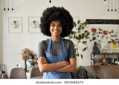 Happy African American young woman with Afro hair modern cafe small business owner, female waitress in reopened restaurant looking at camera standing arms crossed in cozy cafe interior. Portrait.