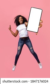 Happy african american young woman showing empty smartphone screen while jumping up over pink studio background, collage, full size photo. Excited black lady recommending nice mobile application